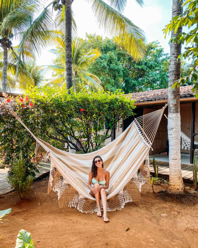 Livía Pereira na Pousada Alquimista sentada numa rede sorrindo num dia de sol aberto - Quanto custa Viajar para Fernando de Noronha