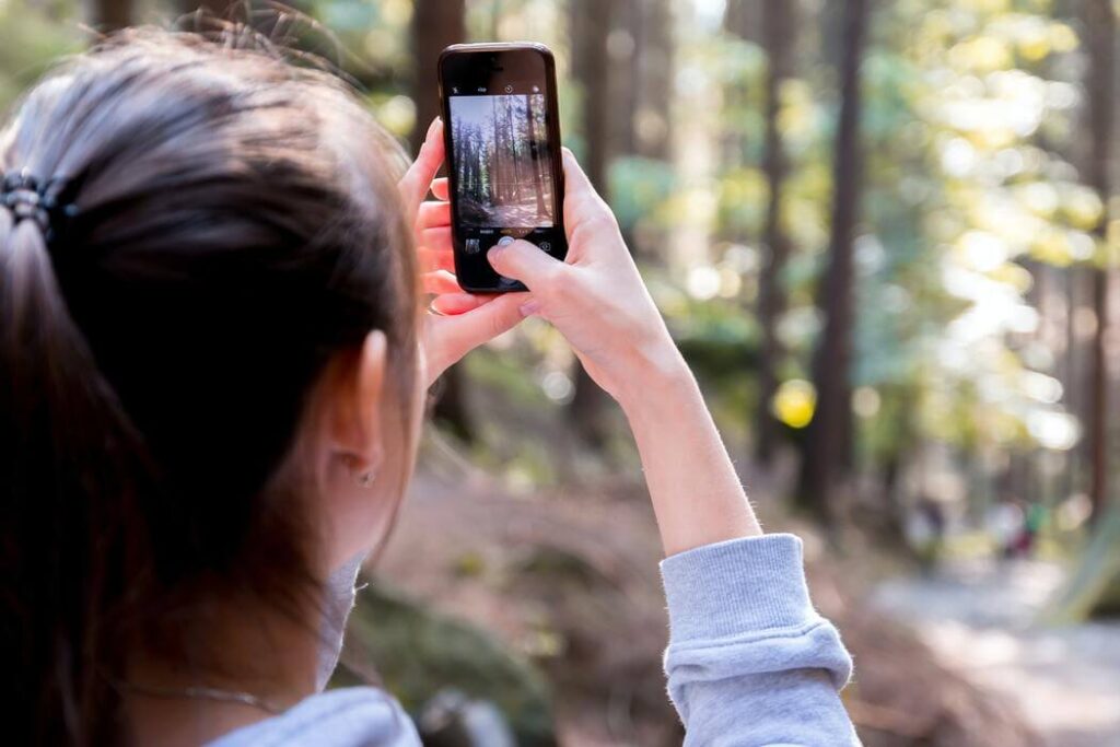 Mulher de cabelos pretos e rabo de cavalo segura o seu celular para tirar foto na floresta
