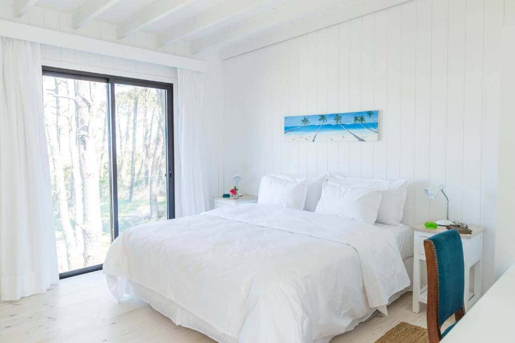 Casa Flor, quarto com cama de casal, varanda, almofadas, luminária, quadro, cadeira, uma ótima opção de onde ficar em Punta del Este no Uruguai