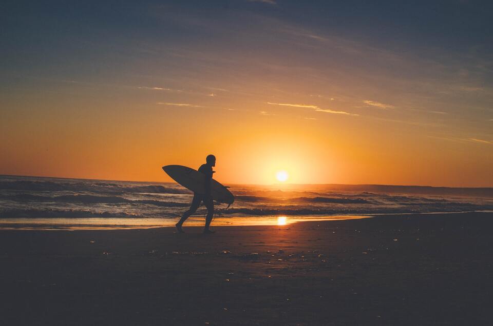 Pôr do sol e um surfista andando pela praia no Uruguai