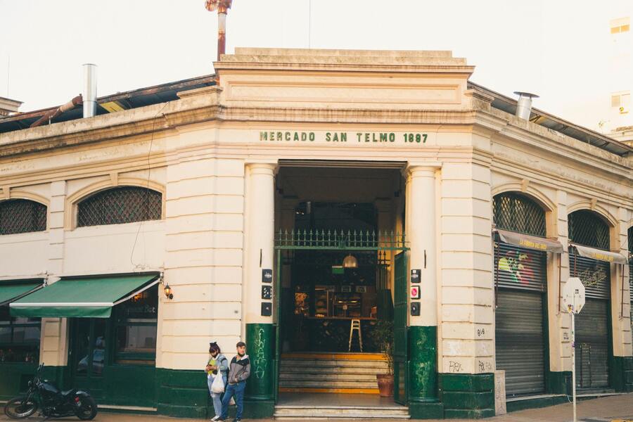 Frente do Mercado San Telmo em Buenos Aires na Argentina com duas pessoas na porta, uma mulher olhando o celular e uma moto estacionada