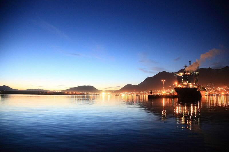 Canal Beagle em Ushuaia, na Argentina, durante o fim da tarde com a parte urbanizada de luzes acesas e um barco navegando no mar. Reprodução: Tripadvisor.