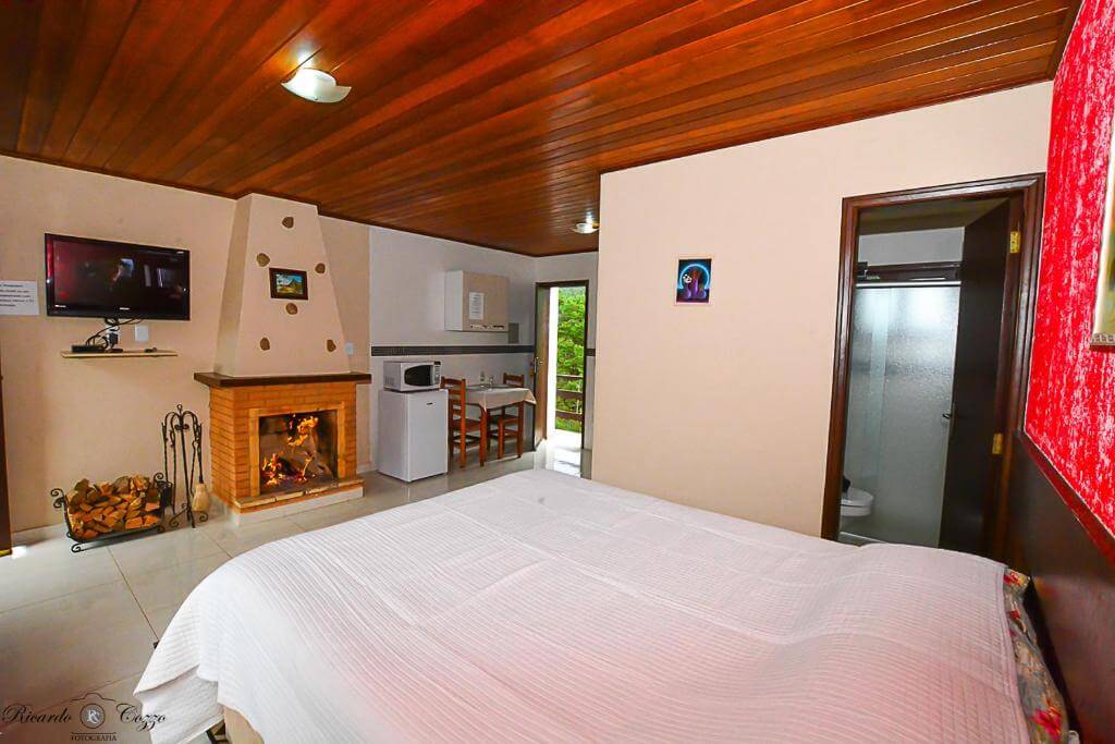 Quarto do Chalé Leopoldo, em Monte Verde - MG, com cama de casal, banheiro, figobar, microondas, mesa, cadeiras, televisor de tela plana