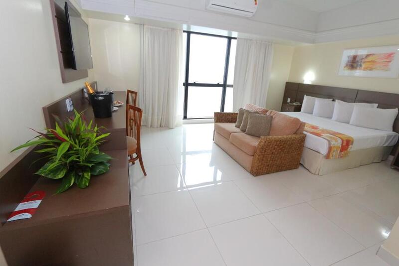 Quarto do Hotel Tropical Executive, em Manaus no Amazonas, com cama de casal, sofá, travesseiros, mesa de escritório, televisão de tela plana e ar-condicionado