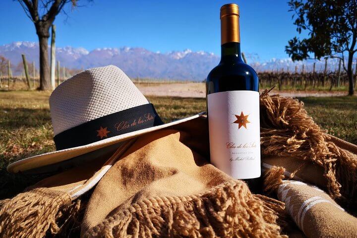 Chapéu, garrafa de vinho e cachecol num dia de sol em um campo abertorepresentando vinícolas em Mendoza na Argentina