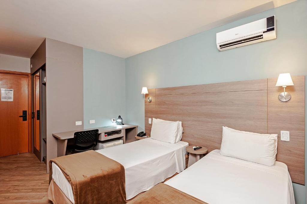 Quarto do Hotel Slim Curitiba Alto do XV, em Curitiba no Paraná, com camas de solteiro, mesa e cadeira de escritório e ar-condicionado