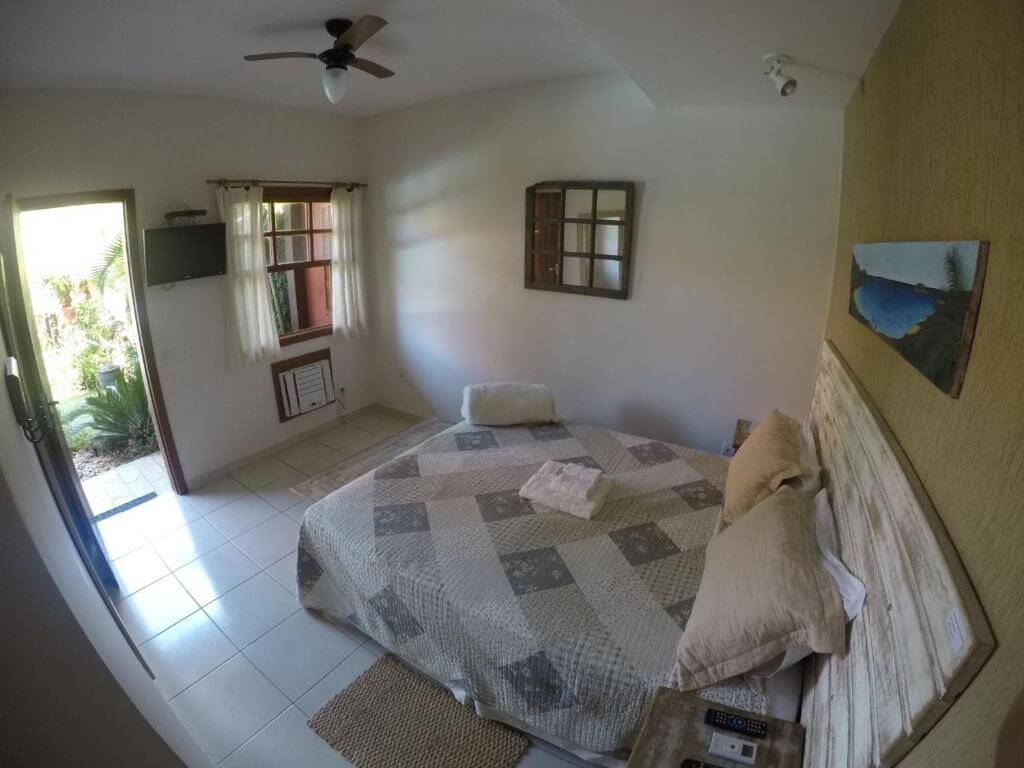 Quarto da Pousada Casa da Aroeira, em Búzios no Rio de Janeiro - RJ, com cama de casal, travesseiros, televisão de LCD, ventilador de teto, e ar-condicionado