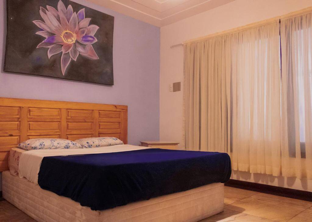 Quarto do The Eco Palace Hostel, em Búzios no Rio de Janeiro - RJ, com cama de casal, travesseiros e quadro onde está pintada uma flor