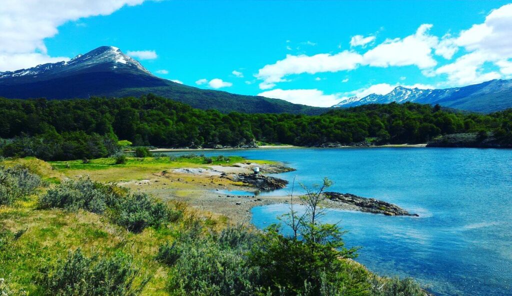 Onde ficar em Ushuaia. Vista do monte arborizado em Ushuaia na Argentina com um belo lago em um dia de sol e céu azul com nuvens. Reprodução: Tripadvisor.