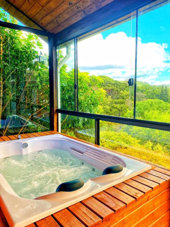 Banheira de hidromassagem para duas pessoas, em um deck de madeira, coberto e com paredes de vidro para admirar a vegetação.