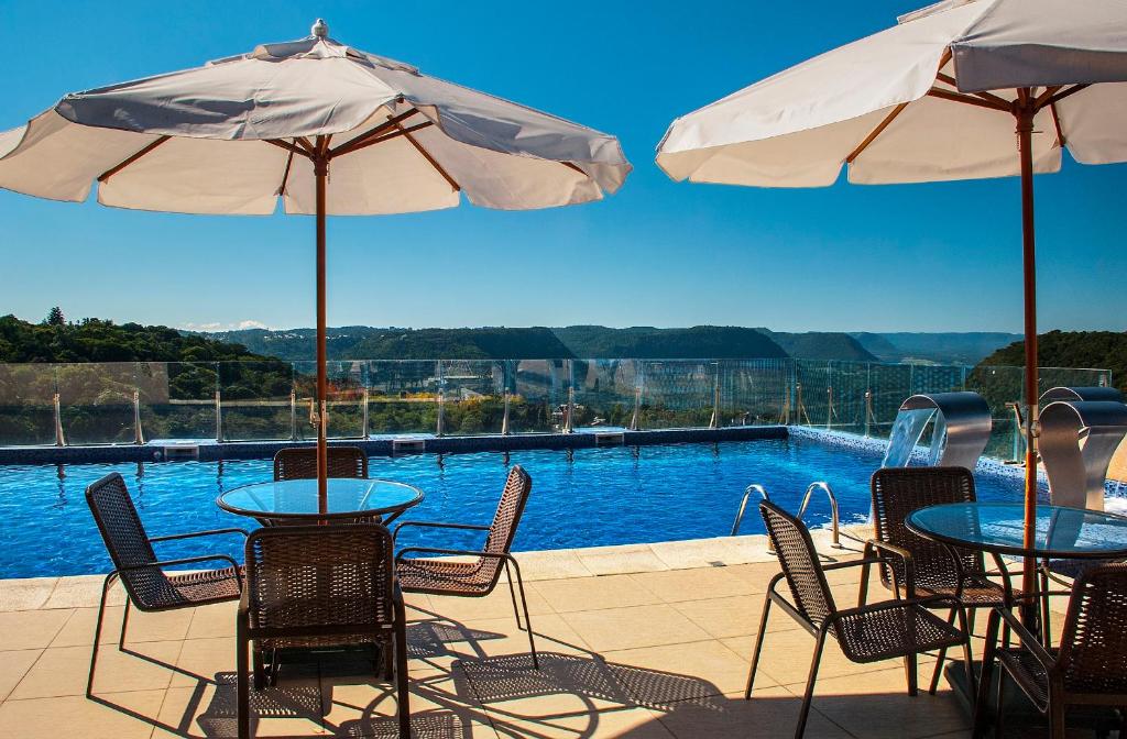 Piscina ao ar livre, com vista das montanhas ao fundo e mesinhas com guarda-sóis.