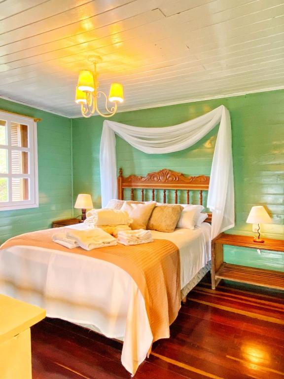 Cama de casal com travesseiros, almofadas e roupa de banho. A parede em verde e o teto em branco. Chão de madeira em hotéis em Gramado petfriendly.