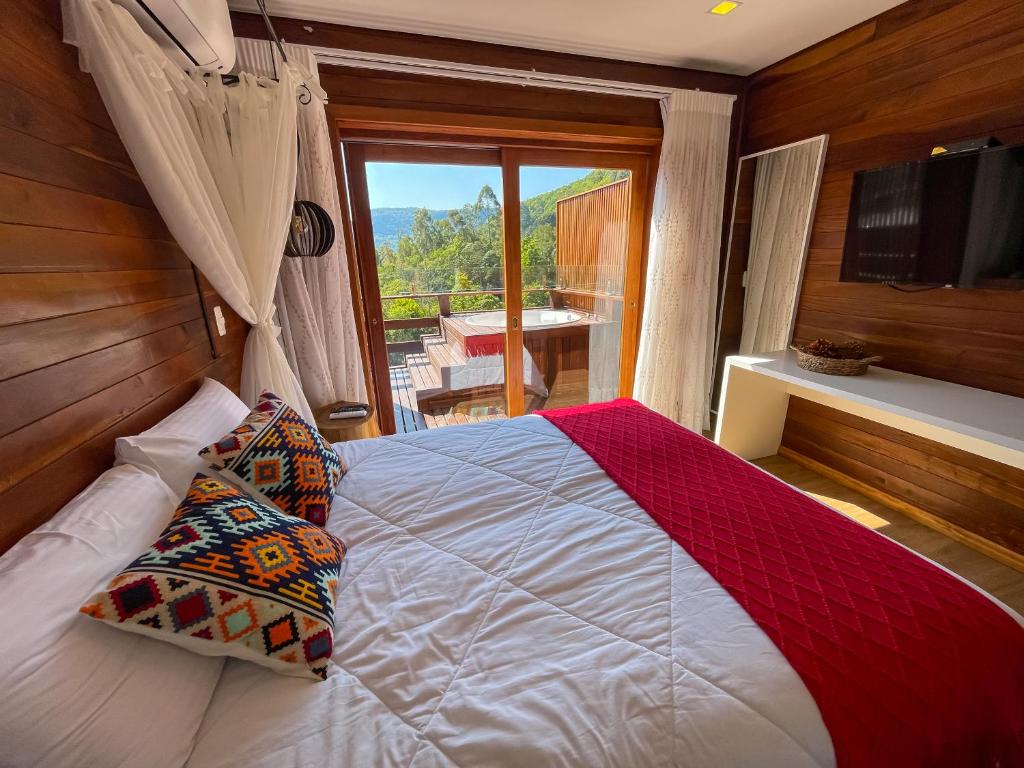 Suíte de casal, ao lado da cama tem um janelão para a varanda em deck de madeira com hidromassagem e vista das montanhas. Hotéis em gramado petfriendly.