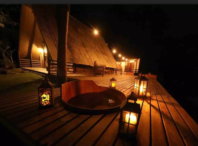 Ofurô em um deck de madeira, de noite, iluminado por velas. Cabanas no interior de São Paulo.