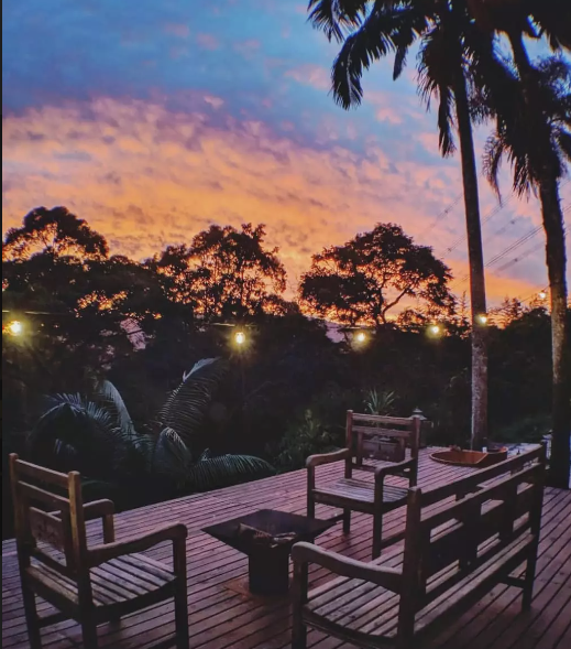 Pôr do sol do deck de madeira com cadeiras e visual das árvores. 