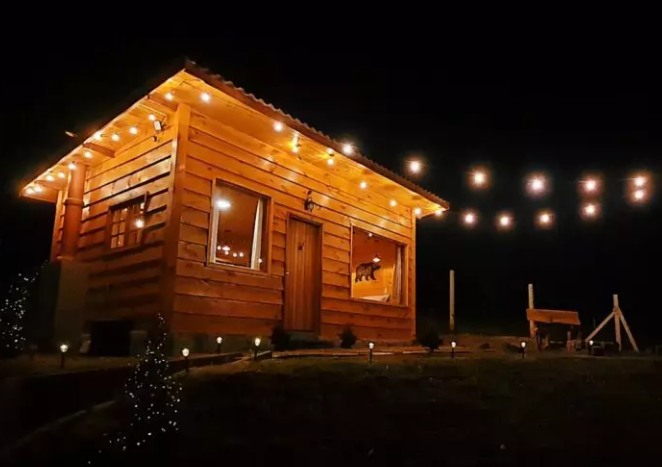 Cabana em madeira, de noite, com luzinhas na área externa