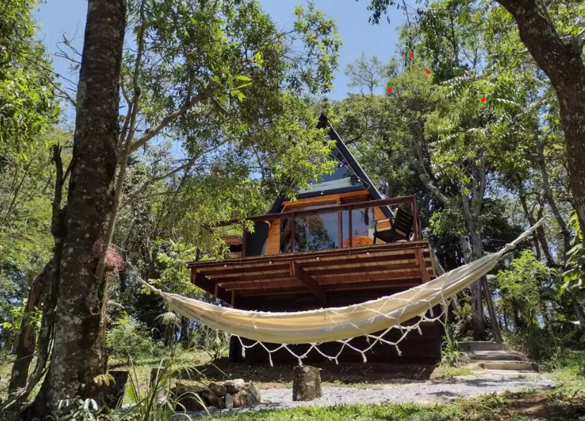 Fachada da Cabana em estilo alpino, com uma rede no andar de baixo e a vista para a varanda. 