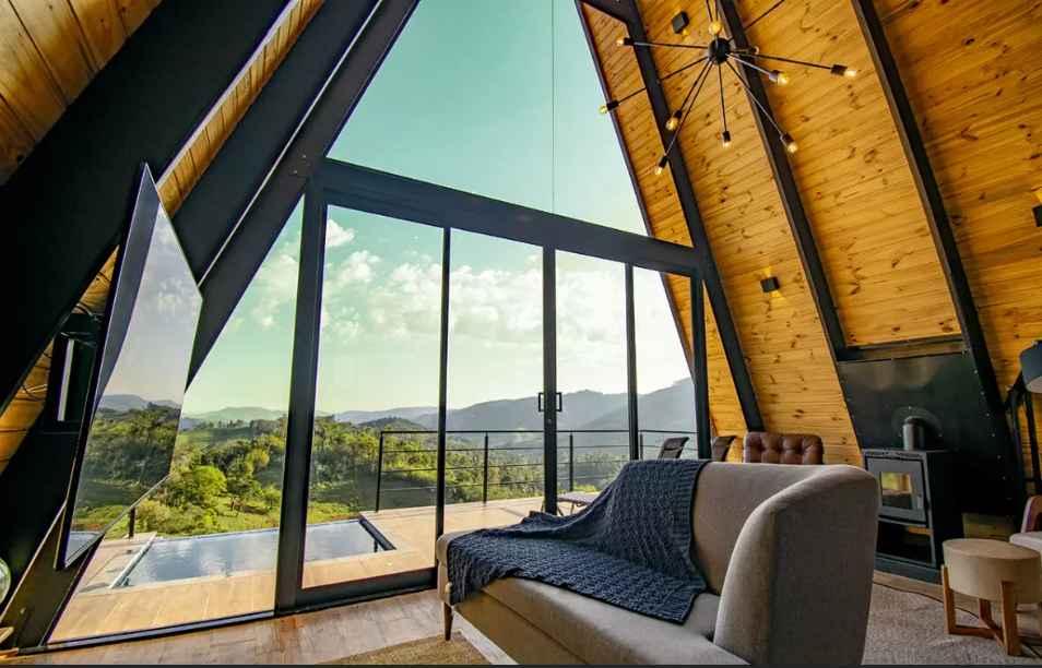 Vista de dentro para fora da cabana, tem varanda com piscina de borda infinita e paisagem das montanhas.