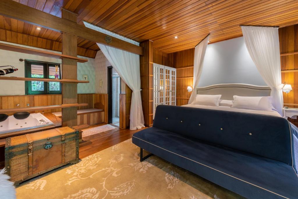 Quarto com cama extra grande, sofá azul, e no cantinho, uma hidromassagem para o casal. Chalés românticos em Monte Verde