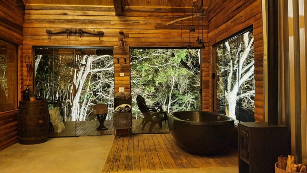 Banheira de imersão em chalé de madeira, com luz ambiente e vista para a natureza