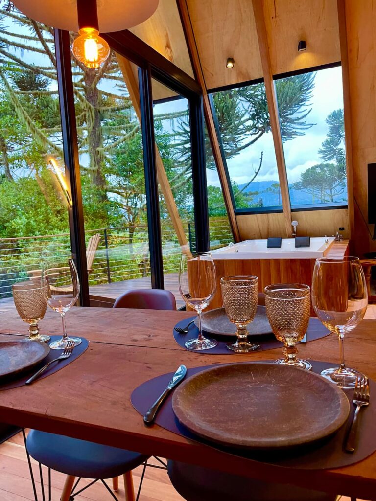 Área interna de chalé, com mesa de para refeições e hidro com vista para a paisagem
