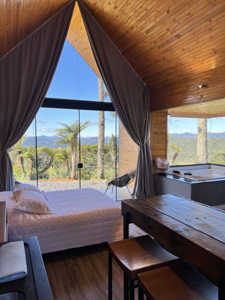 Área interna do chalé com cama de casal, banheira e linda vista das montanhas