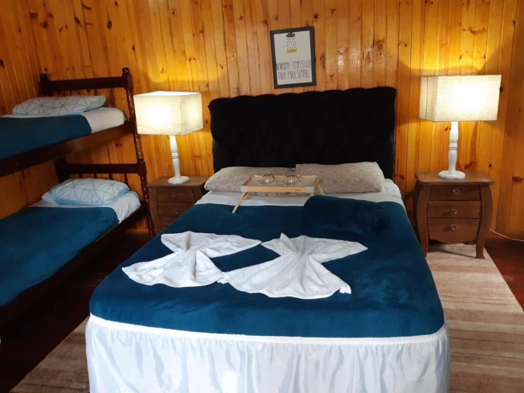 Quarto para família, com cama de casal e uma beliche. O quarto é em madeira, as camas com lençol branco e azul escuro.