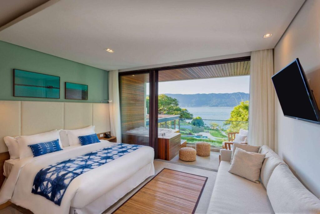 Quarto com cama de casal, sofá e varanda com jacuzzi e vista para o mar em hotéis de luxo Ilhabela