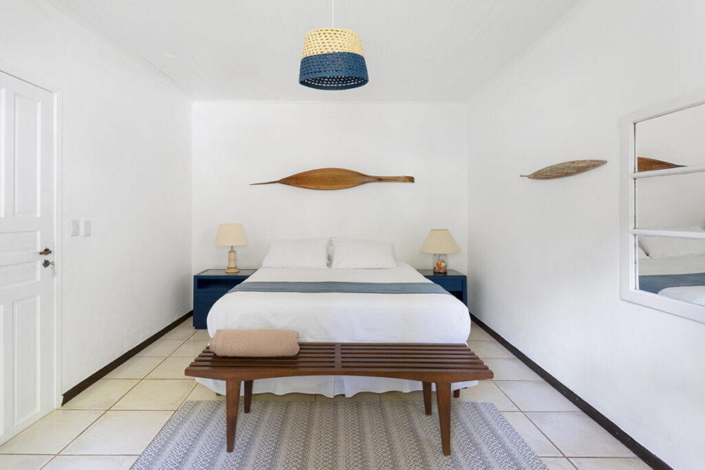 Quarto de casal com decoração minimalista em branco e pequenos detalhes em madeira
