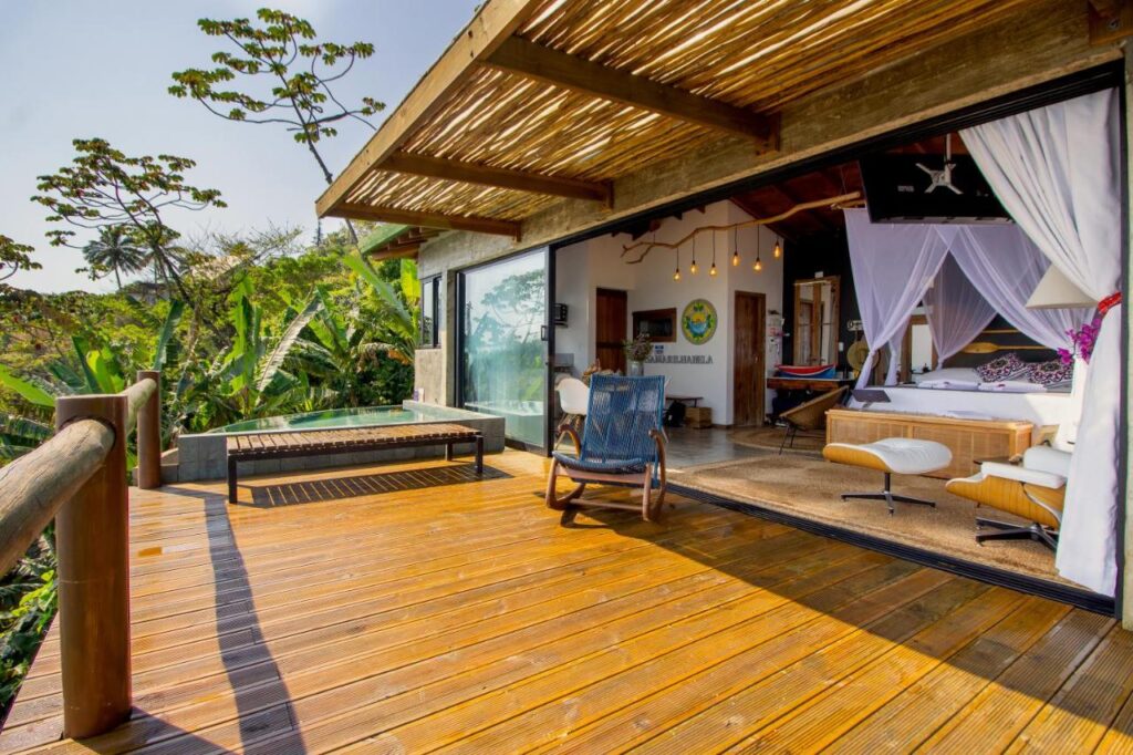 Vista da varanda, em madeira, para dentro da casa, com janelão de vidro que integra os ambientes.