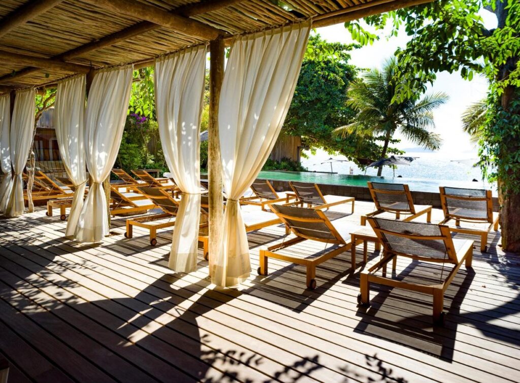 Piscina de borda infinita com vista para a praia e área de deck de madeira coberta em hotéis de luxo Ilhabela