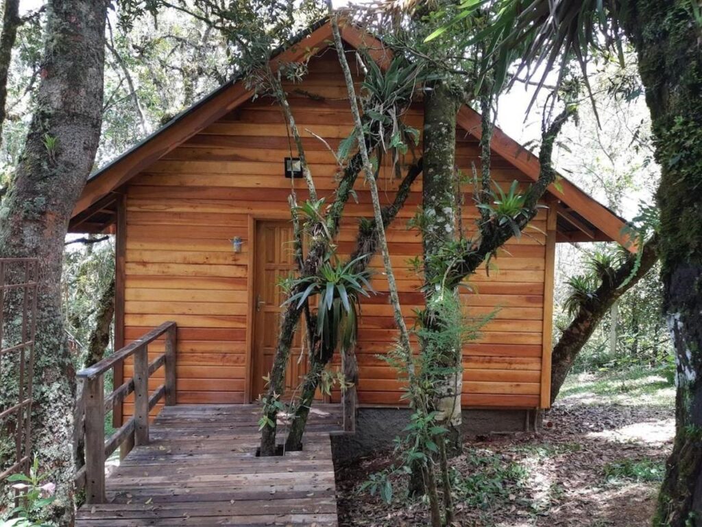 Fachada do chalé beija flor em Campos do Jordão. Casinha em madeira rodeada por árvores.