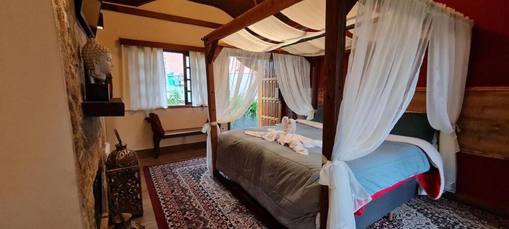 Quarto com cama de casal com mosquiteiro e lareira em frente. Em pousadas com lareira em Campos do Jordão.
