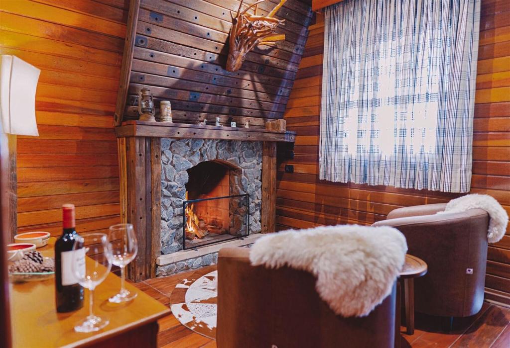 Sala de estar em madeira, com lareira, poltronas e mesa com duas taças e um vinho.