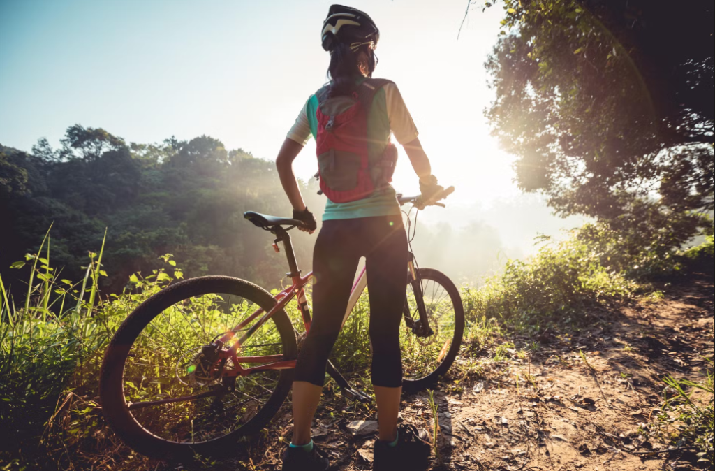 Pessoa admirando o sol apoiada em uma bicicleta, em uma área verde. Passeio de quadriciclo em Monte Verde.