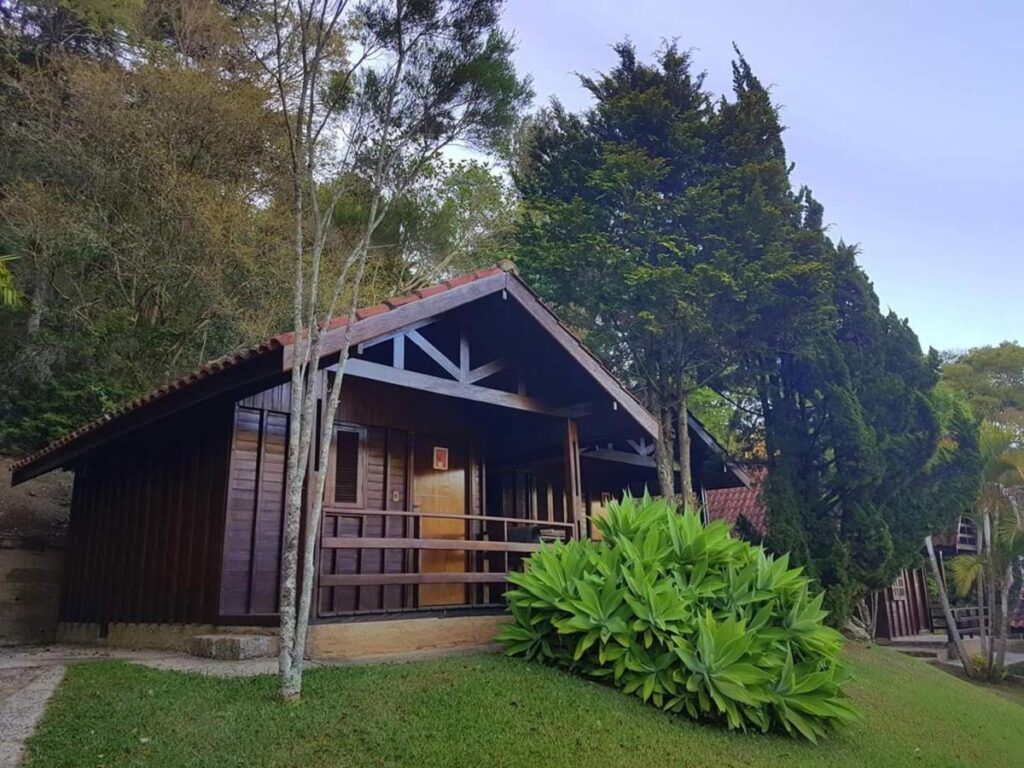 Chalé de madeira rodeado por árvores e um belo jardim em Pousadas Monte Alegre do Sul